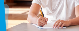 Close-up of learner sitting in a hall and writing in an exam paper.
